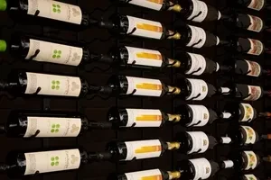 Wall-mounted black metal wine rack displays many wine bottles horizontally.