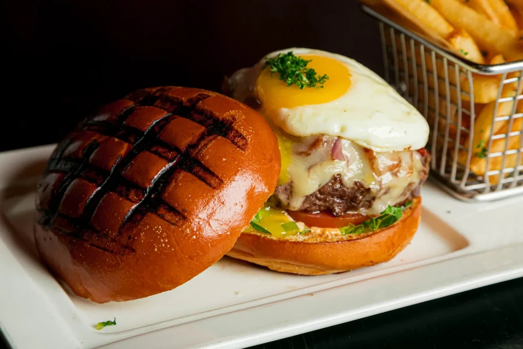 An open-faced burger with runny egg, cheese, and golden fries.