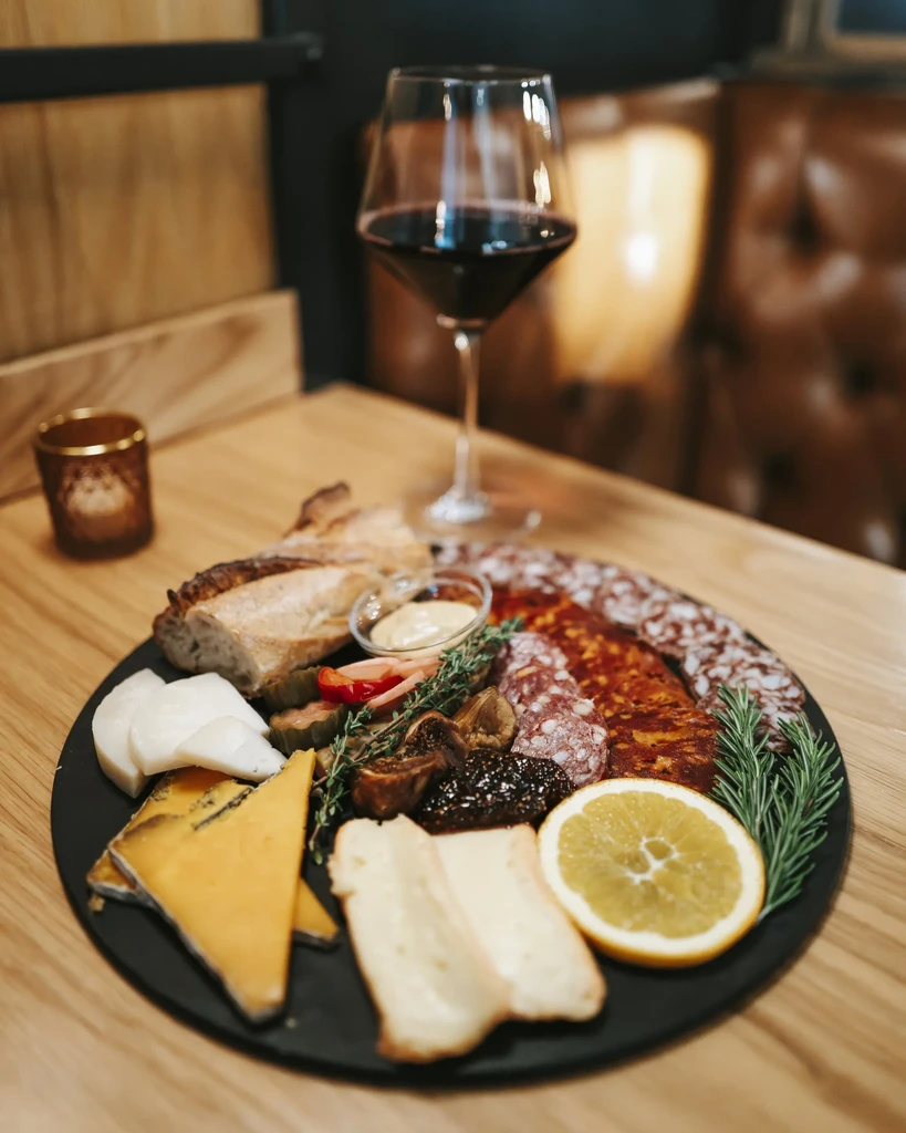 Charcuterie board with cheeses, meats, bread, figs, red wine, candle.