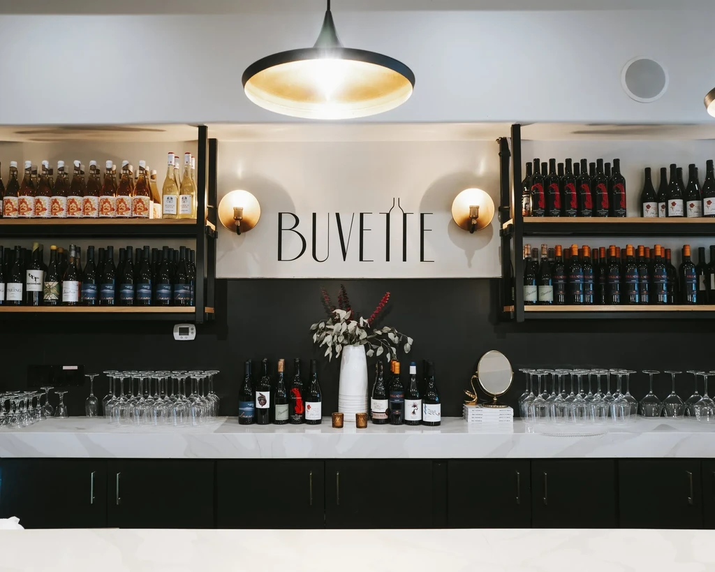 Modern wine bar with neatly arranged glasses, bottles, and 'BUVETTE' sign.