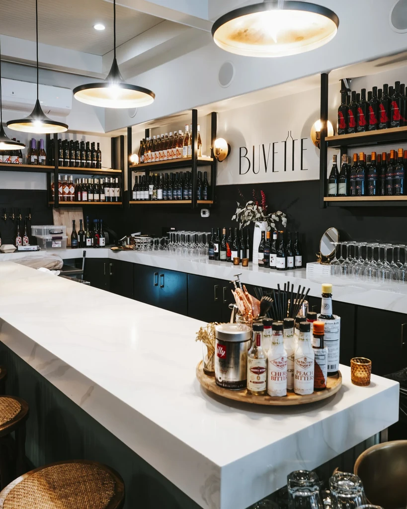 Modern bar with white marble counter, bottles, glasses, and Buvette sign.