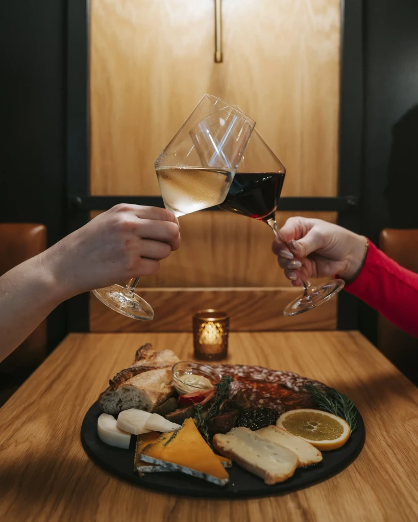 Charcuterie board with cheeses and meats, hands toasting wine glasses.