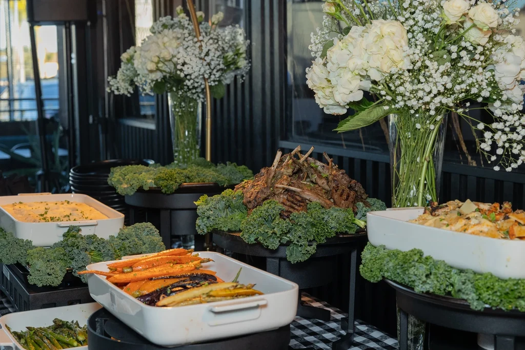 Upscale buffet with lamb chops, roasted carrots, casseroles, and floral arrangements.