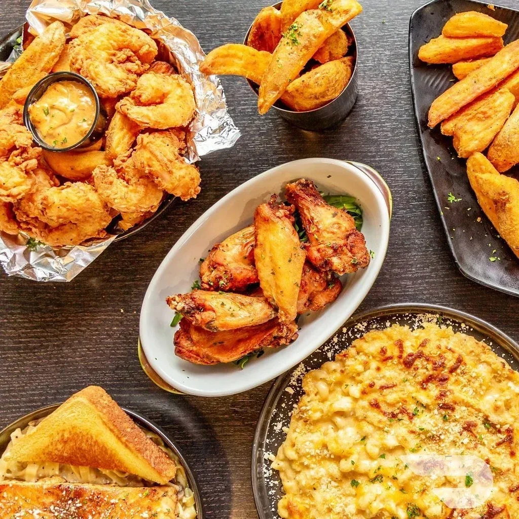 Overhead view of diverse comfort food: fried shrimp, chicken wings, mac and cheese.