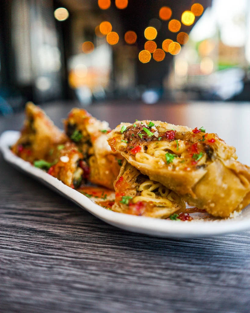 Crispy deep-fried pastries with noodles, red sauce, herbs, chili flakes.