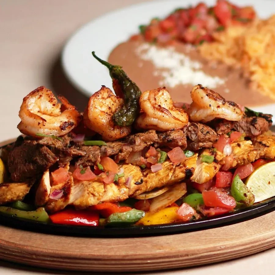Sizzling fajitas platter with shrimp, steak, chicken, peppers, and lime.
