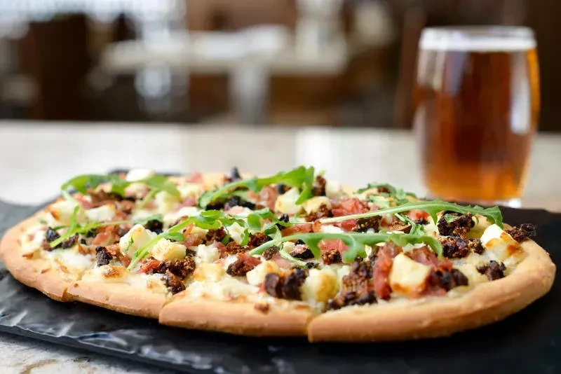Flatbread with cheese, cured meat, arugula, and a glass of beer.
