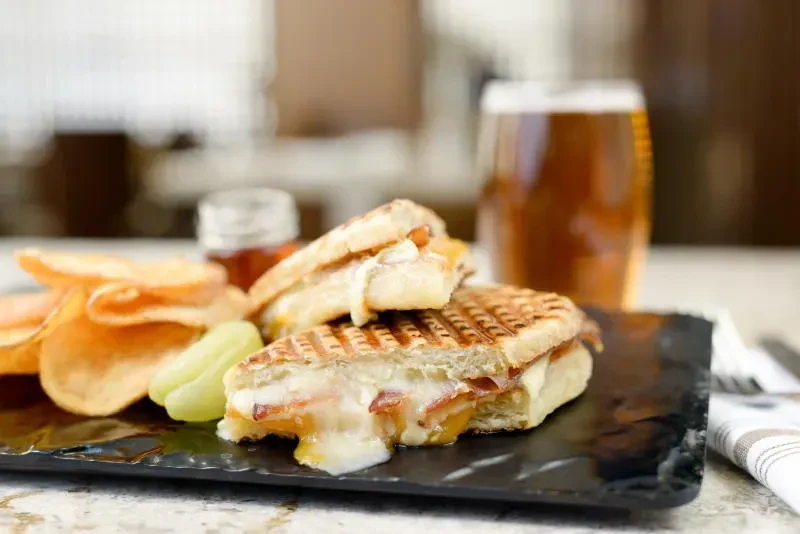 Grilled panini with melted cheese and bacon, chips, and beer.