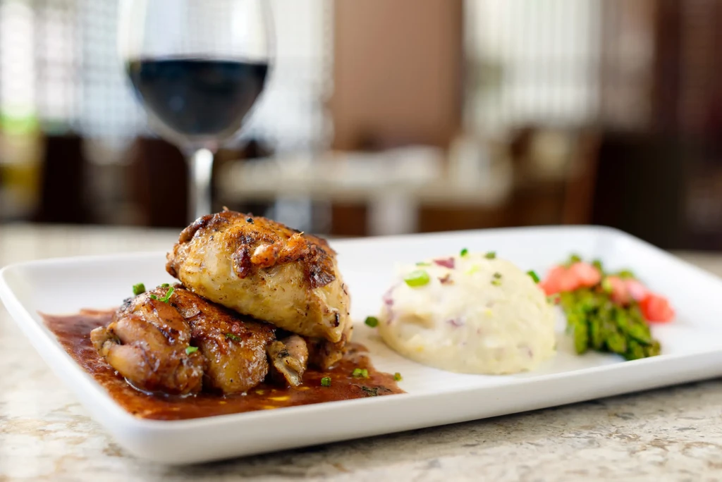 Professionally plated chicken, mashed potatoes, asparagus, radish, and red wine.