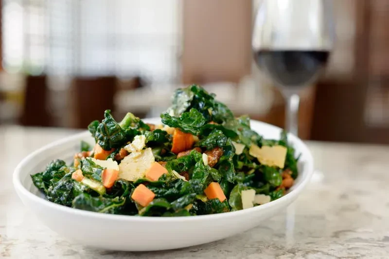 Close-up of a green kale salad with orange vegetables and nuts.