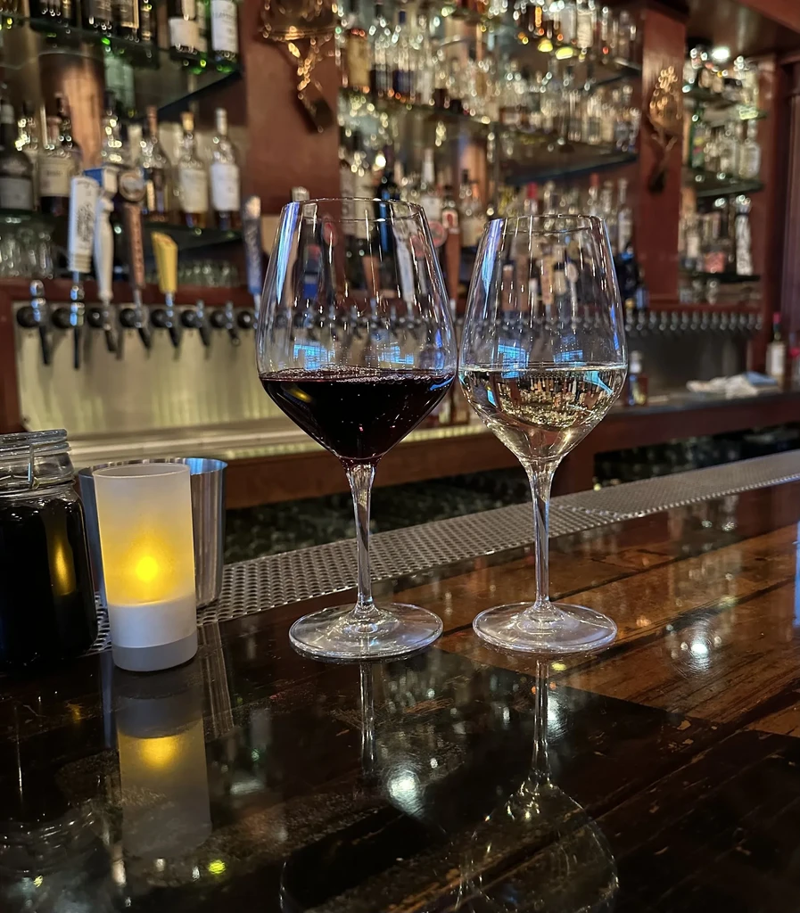 Close-up: Two wine glasses, glowing candle, blurred bar background.