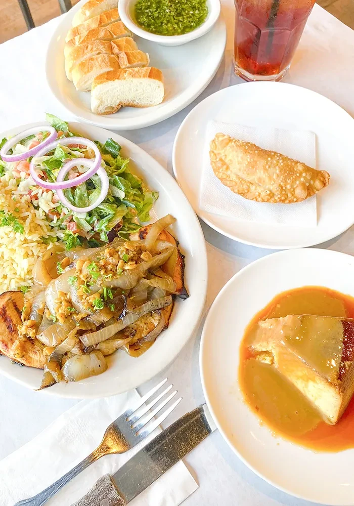 Overhead view of a dining table with grilled protein, rice, salad, and dessert.
