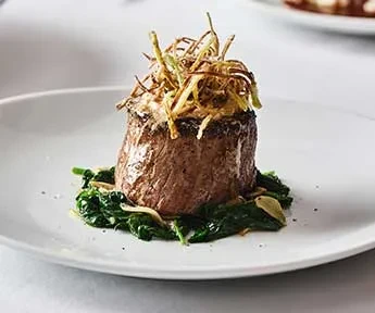 Seared filet mignon, spinach, crispy leeks, and creamy sauce on a plate.