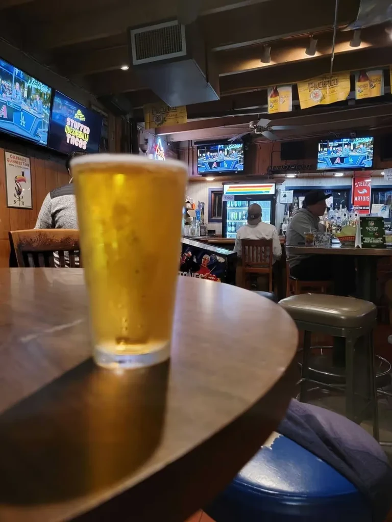 Close-up of amber beer with condensation in a dim sports bar.