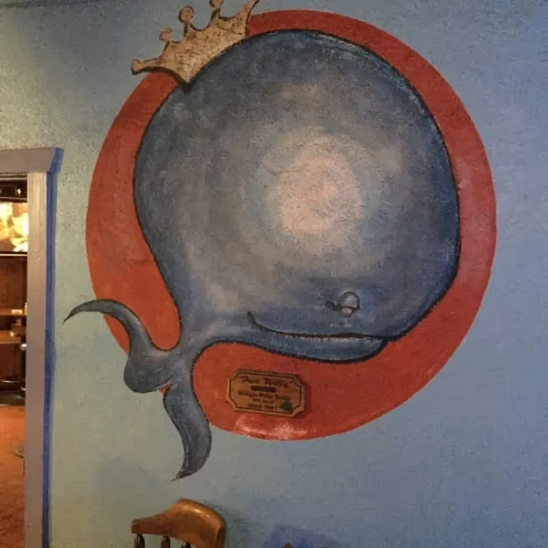 Mural of crowned blue whale with "Poco Willy" plaque in restaurant.