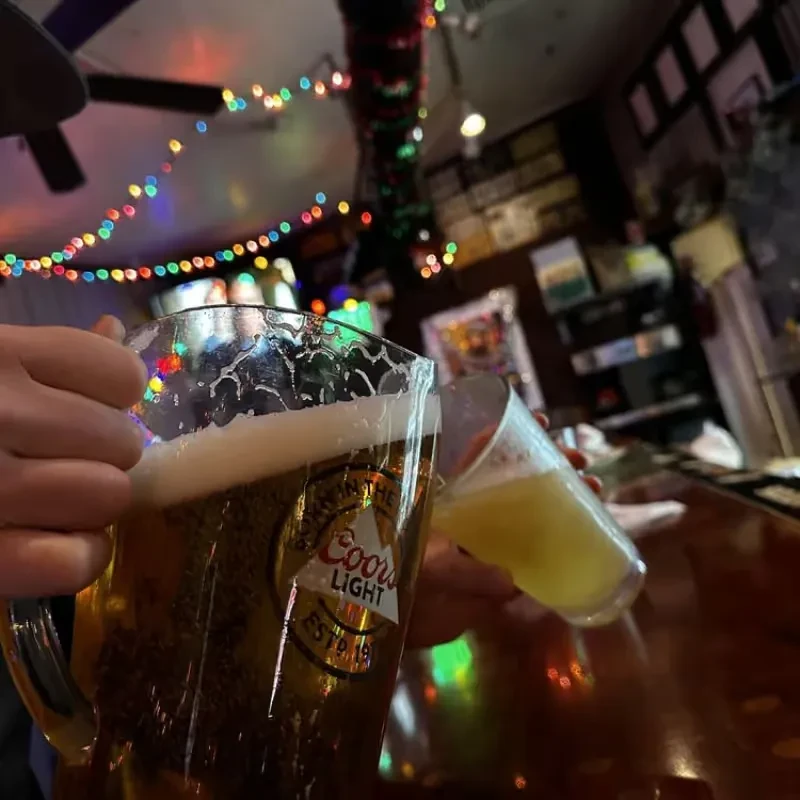 Hands hold a Coors Light pitcher and drink in a festive bar.