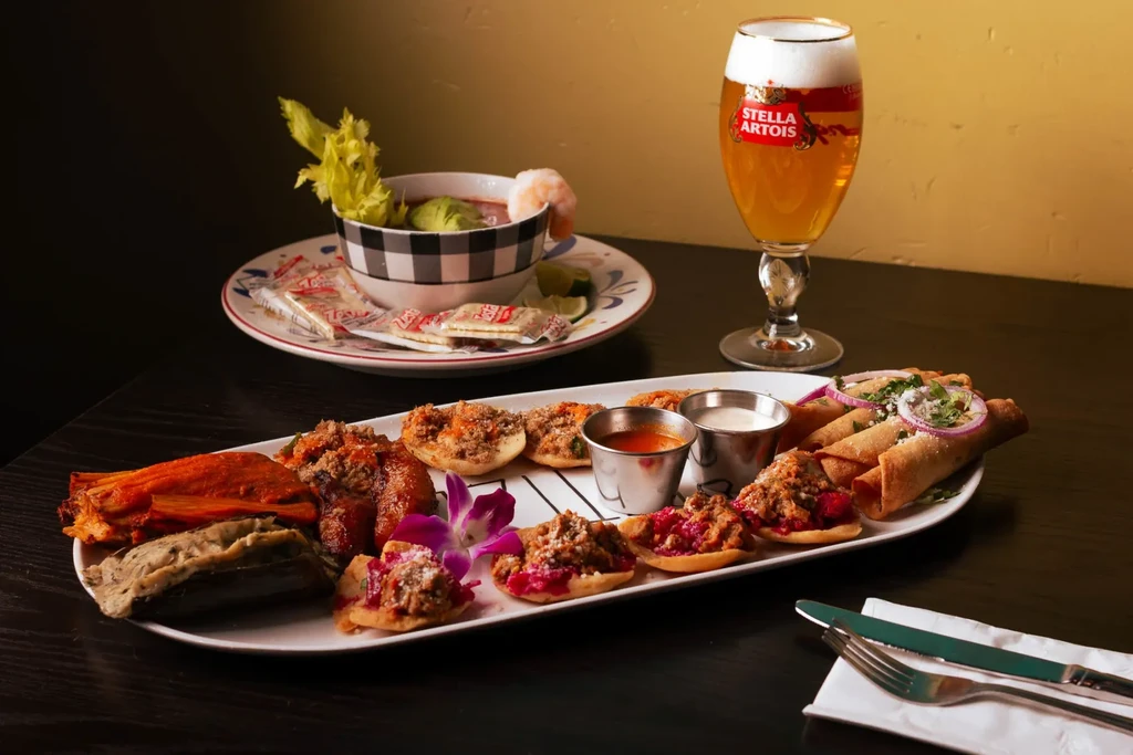Table laden with varied appetizers, shrimp cocktail, and Stella Artois beer.