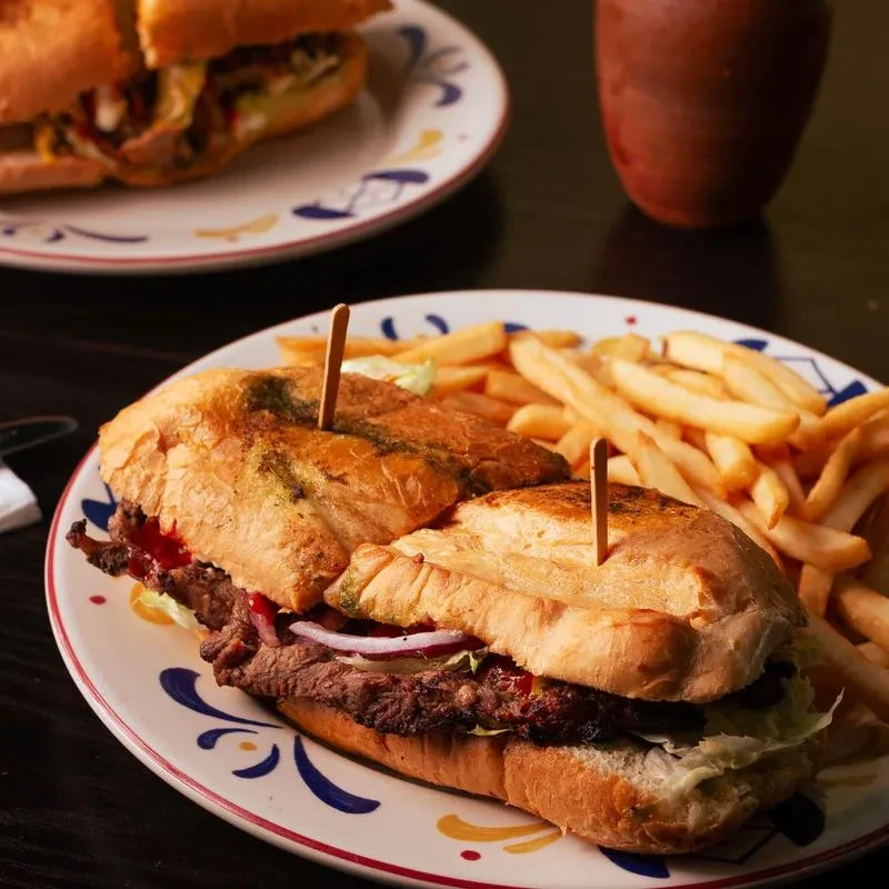 Halved grilled meat sandwich with lettuce, onion, sauce, and fries.