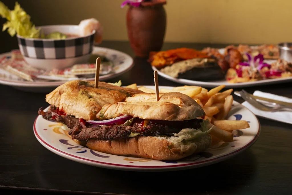 Large sub sandwich, french fries, and various dishes on a dark table.