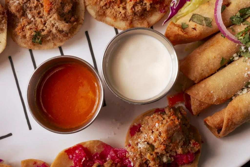 Overhead: Appetizer platter with fried rolls, topped flatbreads, and two sauces.