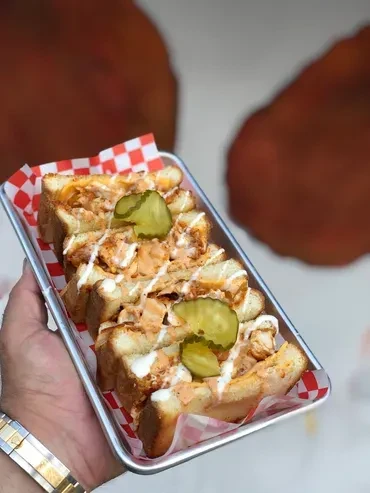 Grilled sandwiches with creamy filling and pickles in a red checkered tray.