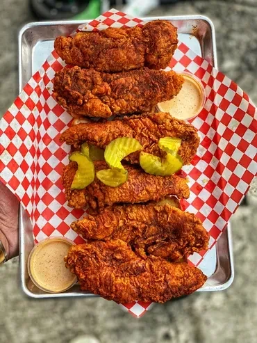 Crispy fried chicken in metal tray with pickled jalapeños and sauces.