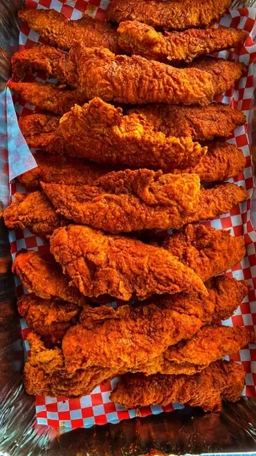 Crispy golden chicken tenders in a foil tray with checkered paper.