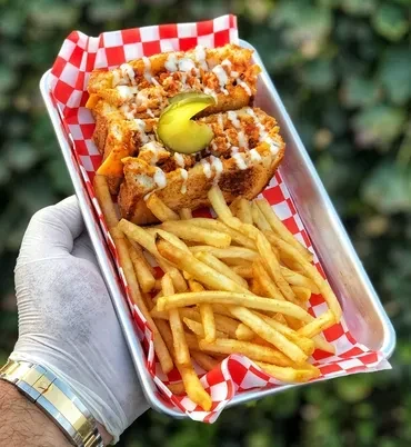 Gloved hand holds a tray of loaded sandwiches, fries, and a pickle.