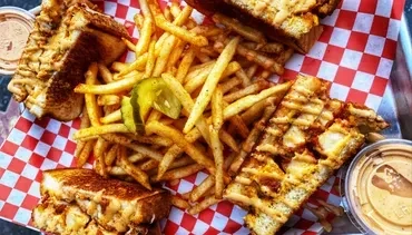Grilled sandwiches, seasoned fries, pickle, and dipping sauces on a tray.