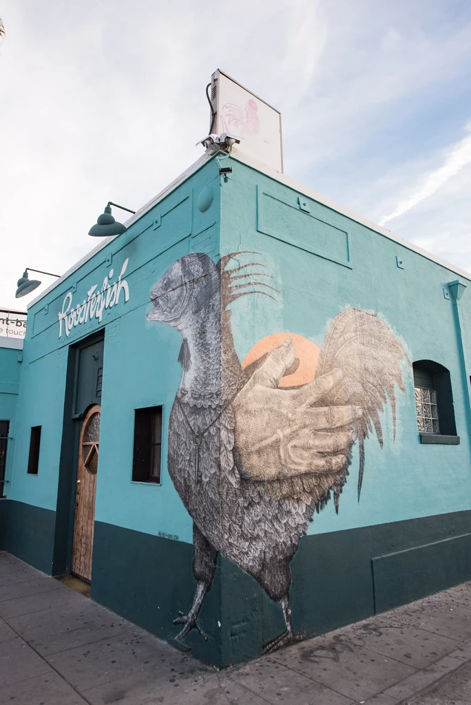 Two-tone teal Roosterfish building features a fish-bird mural and sign.