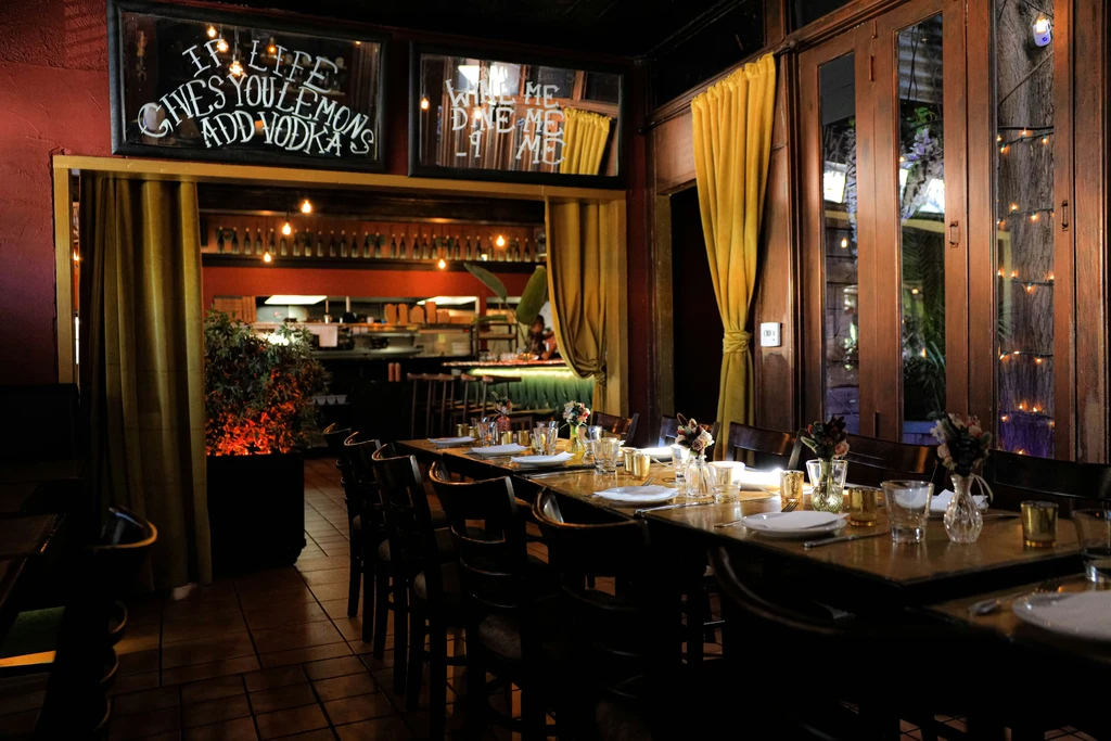 Warm restaurant interior with dining table and "Lemons Add Vodka" sign.