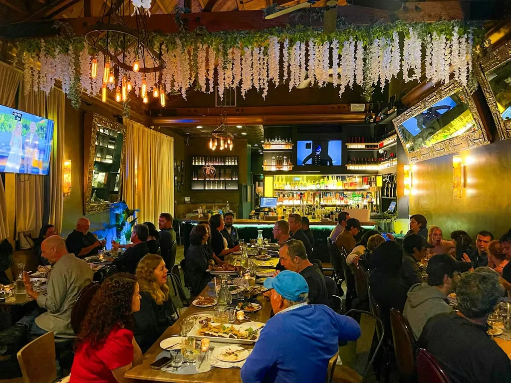 Bustling restaurant interior with warm lighting, floral garlands, and many patrons.