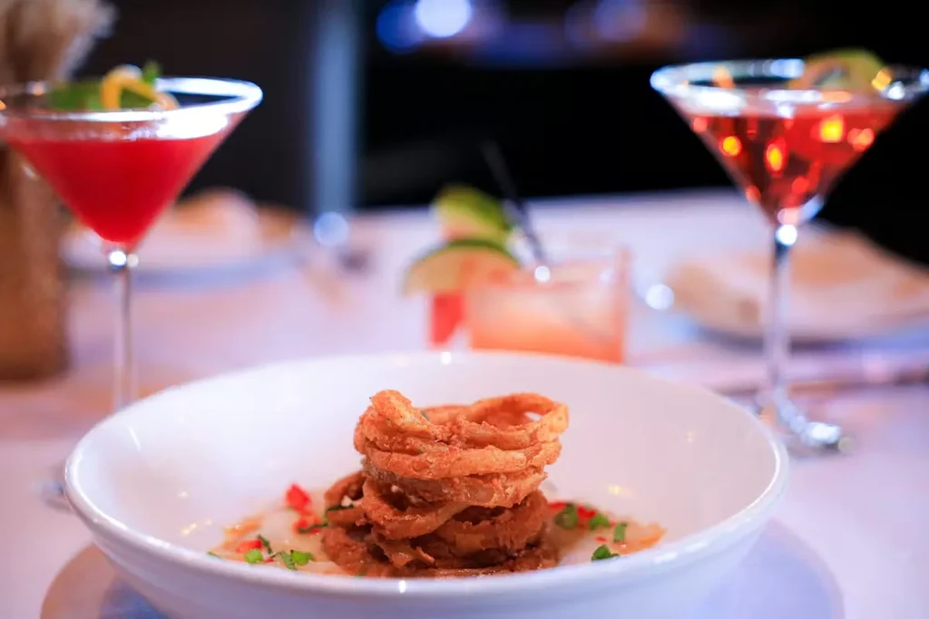 Crispy onion rings, creamy sauce, and two red cocktails on a table.