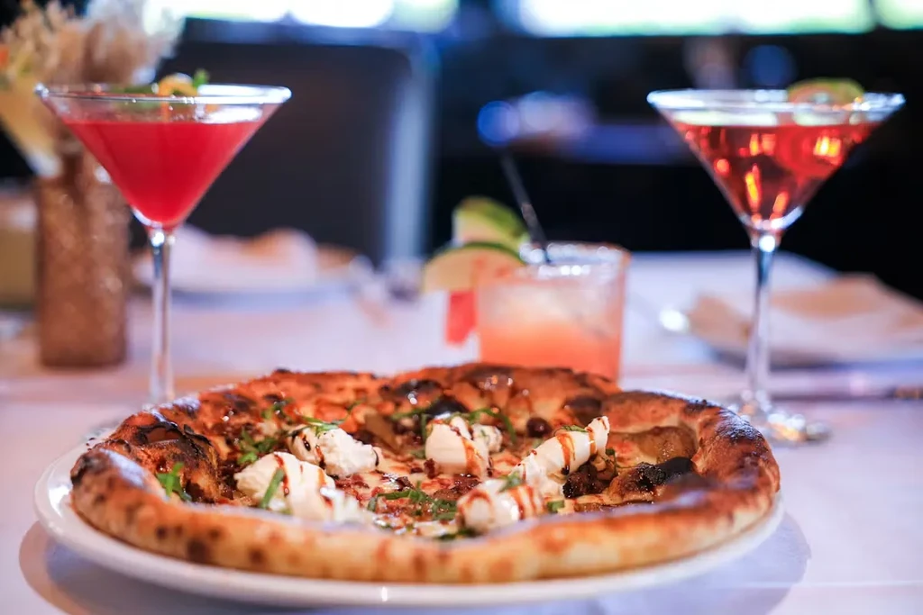 Gourmet pizza with cheese and herbs, three cocktails on white cloth.