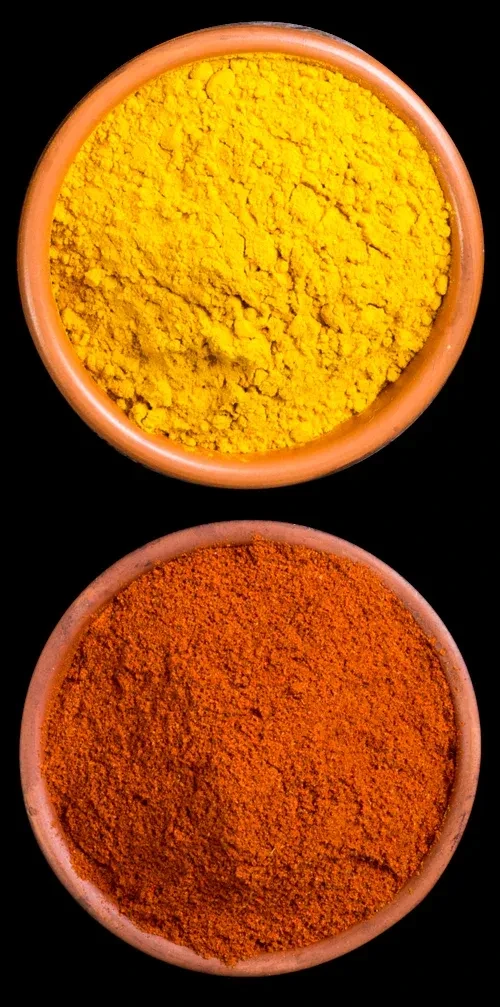 Two clay bowls with yellow turmeric and orange-red chili powder on black.