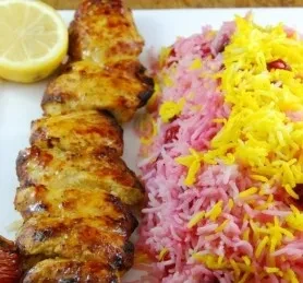 Grilled chicken skewer with colorful rice and a lemon wedge.