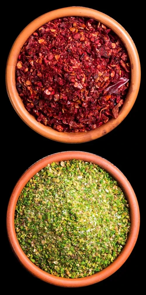 Stacked terracotta bowls filled with vibrant red and green spices.