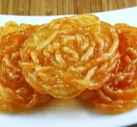 Three intricate, syrupy fried golden-orange desserts on a white plate.