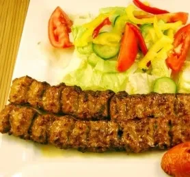 Grilled ground meat skewers and fresh salad on a white plate.