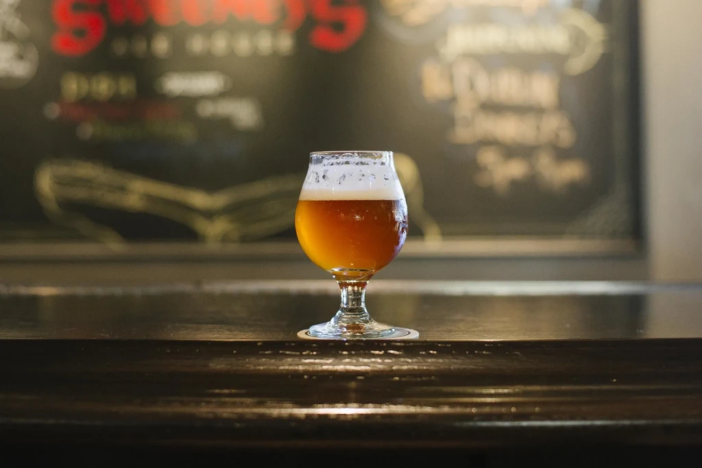 Tulip glass of golden-amber beer with condensation on a dark bar.