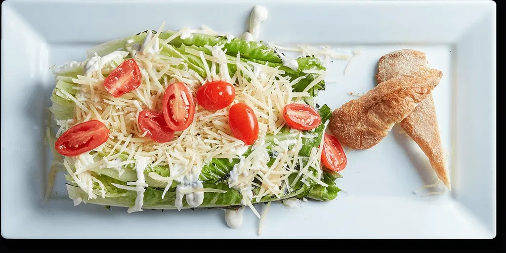 Plated Caesar salad with romaine, Parmesan, cherry tomatoes, dressing, and croutons.