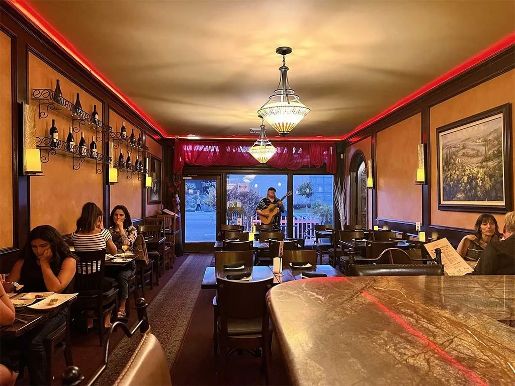 Warmly lit restaurant with dining guests, prominent bar, and live guitarist.