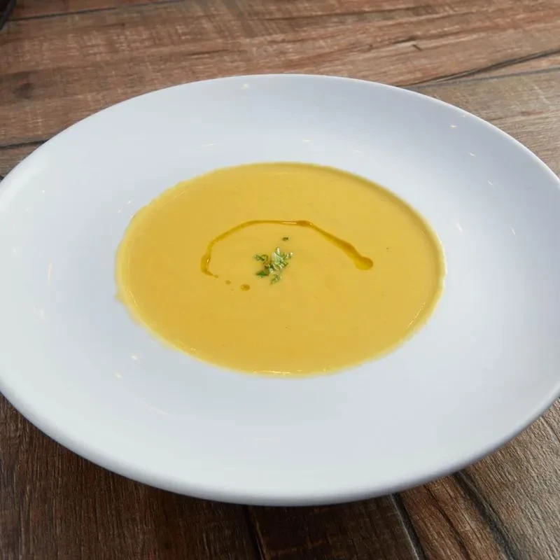 Creamy golden soup with oil swirl and green herbs in white bowl.