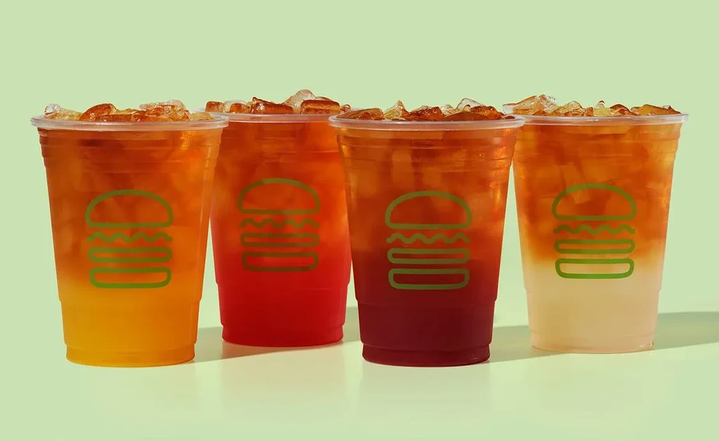 Four plastic cups hold gradient iced drinks with burger logos.