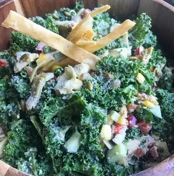 Overhead green kale salad with creamy dressing, seeds, crispy strips.