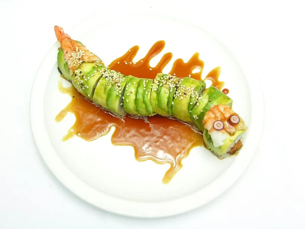 Green avocado sushi roll shaped like a creature with shrimp and eyes.