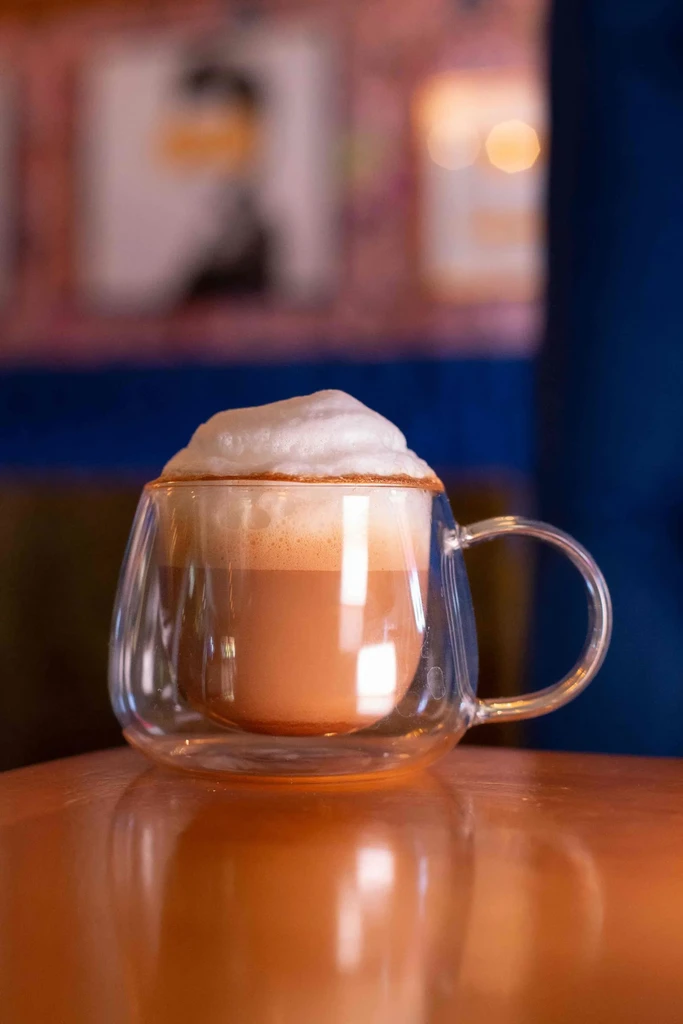 Latte in clear glass mug with overflowing fluffy white foam.