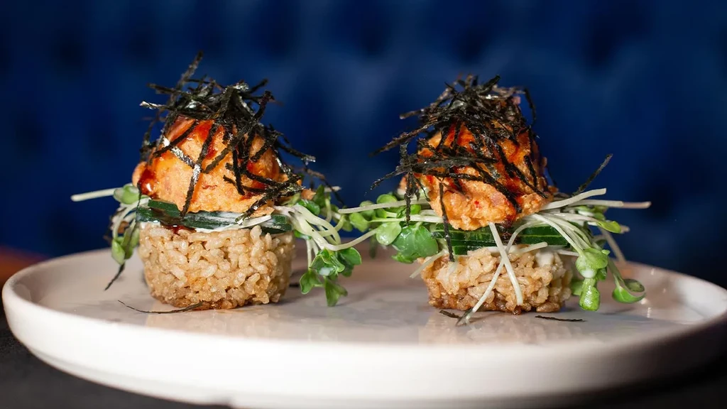 Two plated portions of rice, orange seafood, cucumber, seaweed, sprouts.