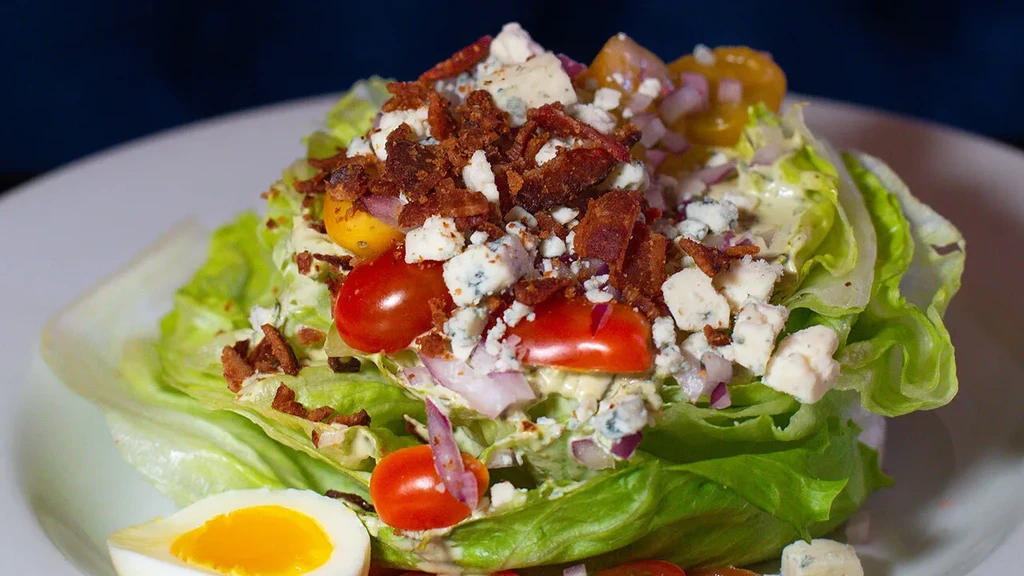 Wedge salad with bacon, blue cheese, tomatoes, and egg on a plate.