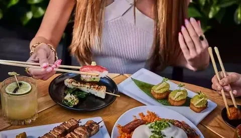 Two people with chopsticks sharing various food plates at a table.